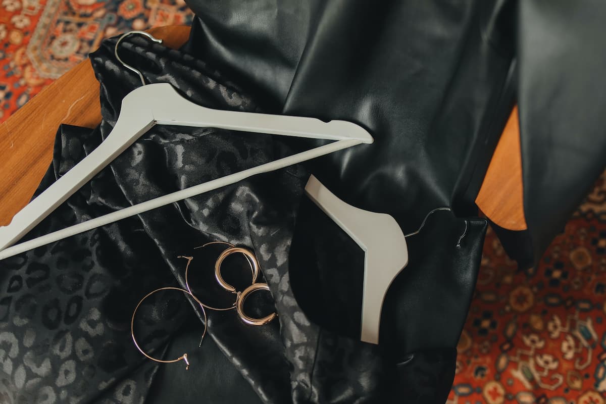 White coat hangers, black clothes, and gold earrings are on the carpeted floor. 