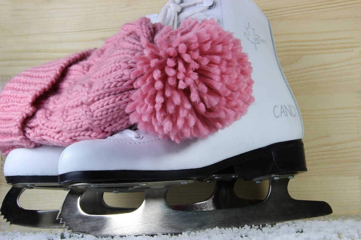Pink-knitted beanie hat on white ice skates on a wooden surface. 