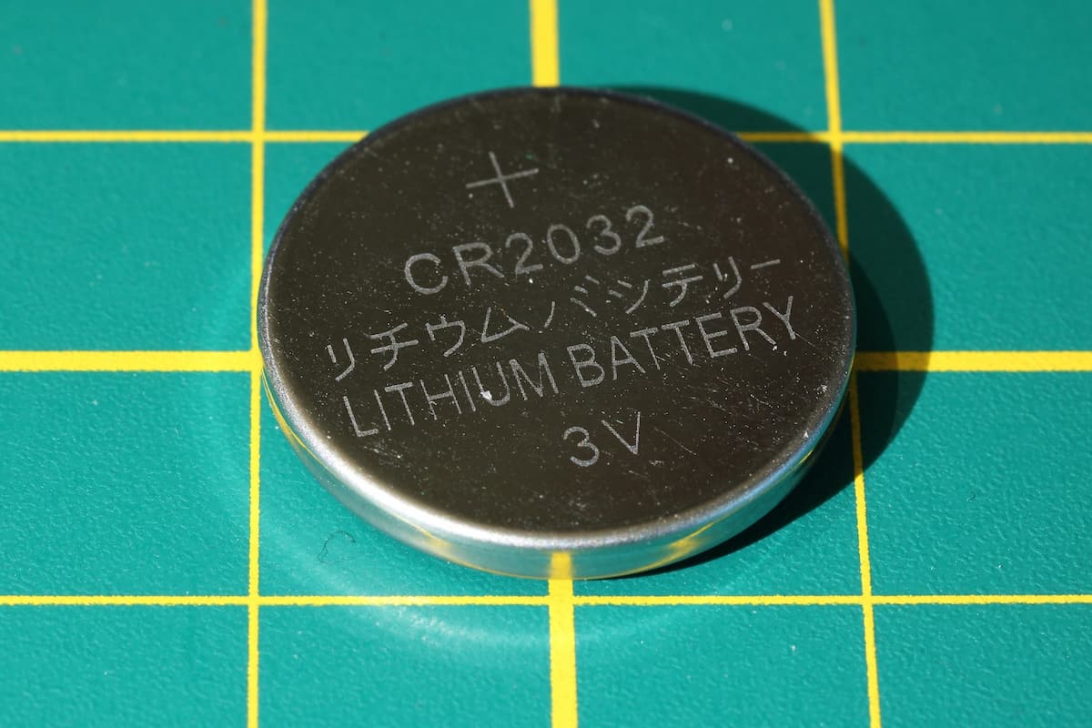 Button-sized cell lithium battery on a green and yellow surface. 