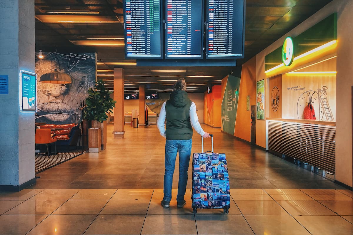 A man is standing while holding luggage inside the airport. 