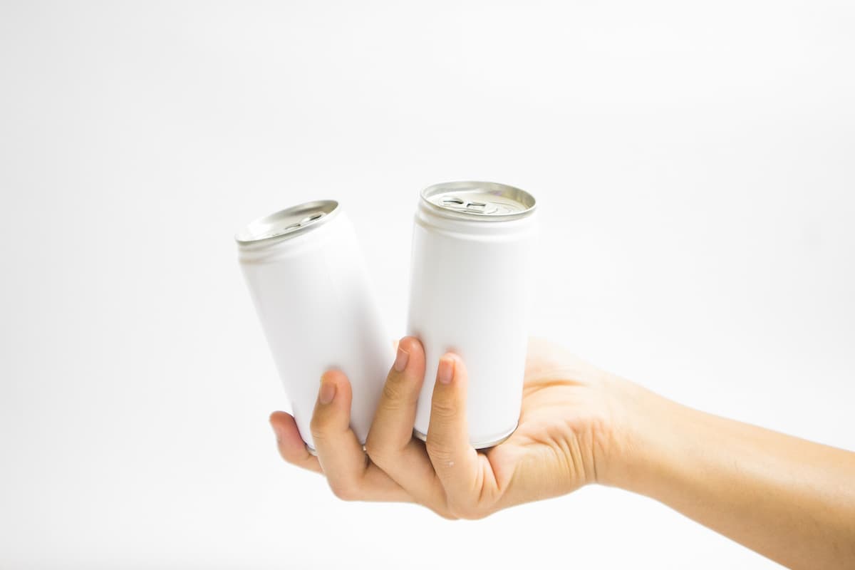 A person's hand holding two white cans on a white background. 