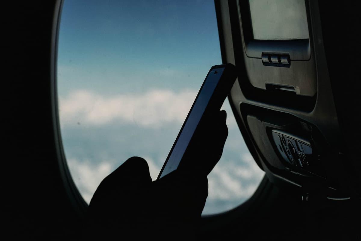 A person holding a smartphone in the airplane with the background of the airplane's window. 