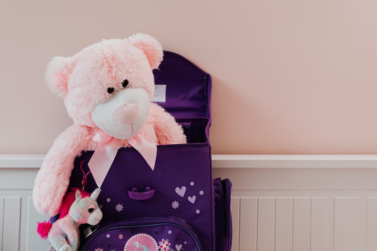 Pink stuffed teddy bear in a purple bag with a stuffed unicorn keychain. 