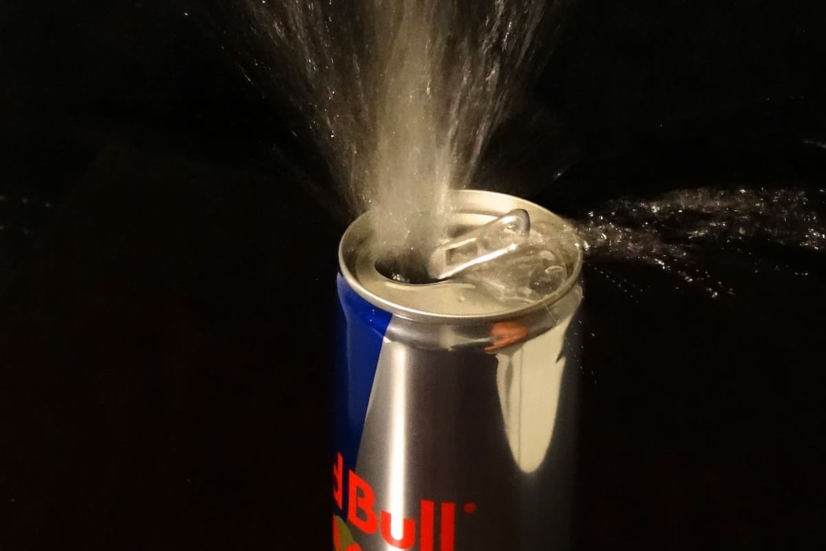 A can of Red Bull energy drink explodes on a black background. 