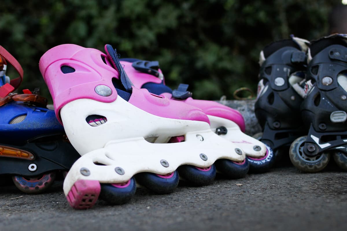 Pink and white rollerblades on the ground together with other rollerblades.