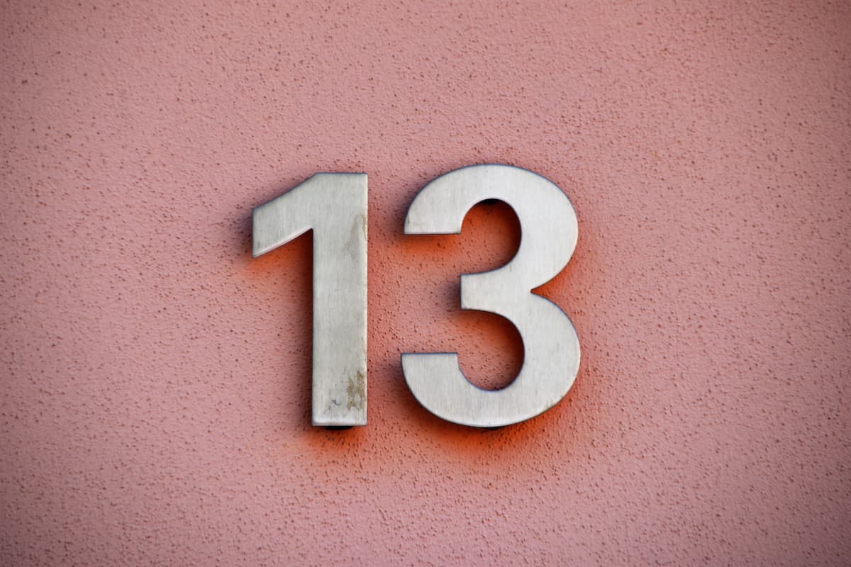 A gray number 13 on an orange wall. 