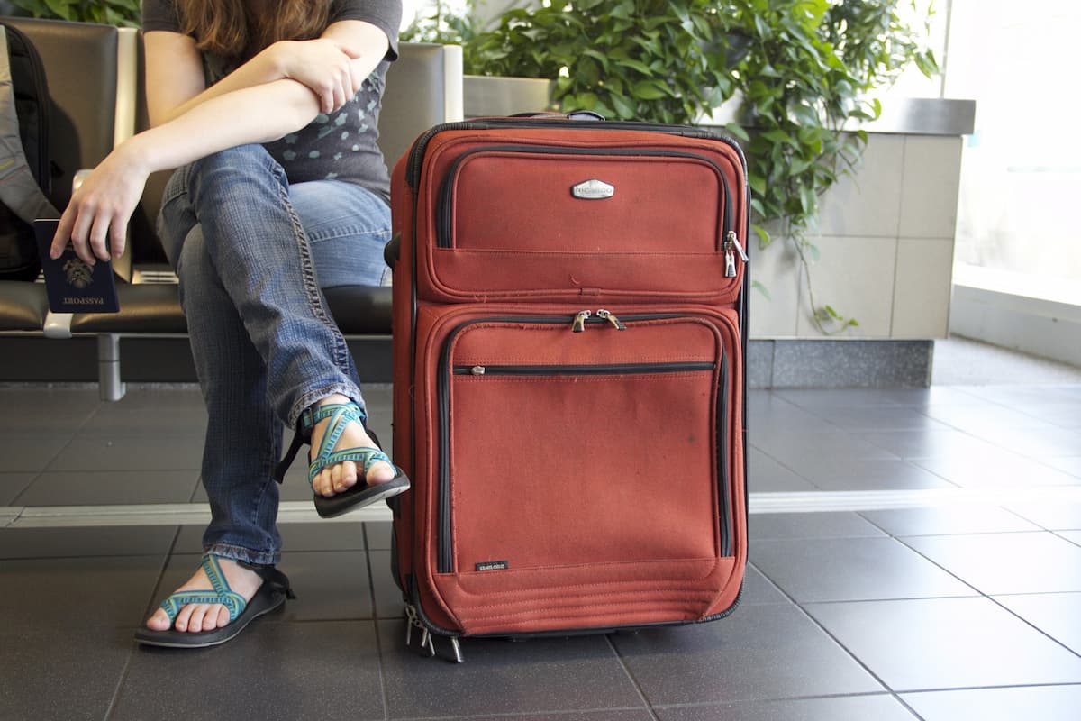A red suitcase beside a person sitting at the airport. 