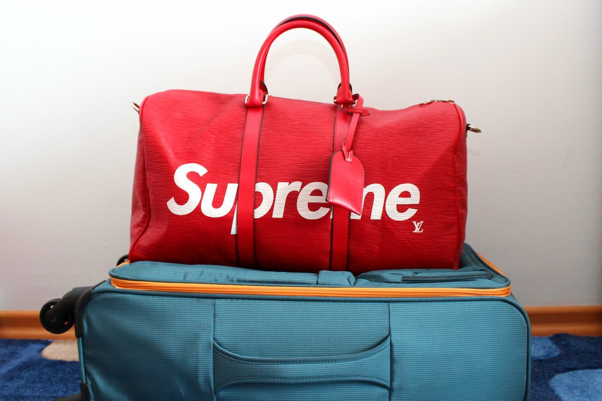 A red Supreme duffel bag on top of a blue suitcase. 