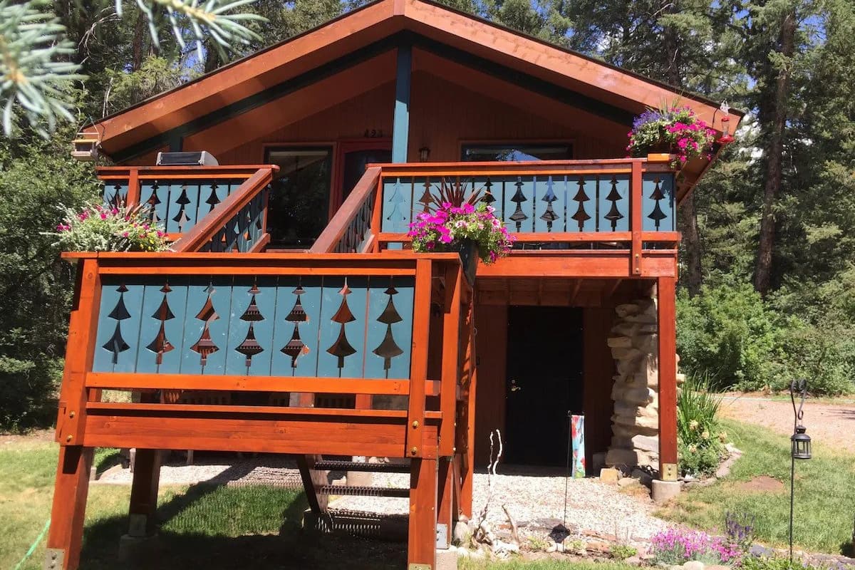 The exterior of A Road Less Traveled Cabin with flowers on the balcony and trees in the background. 