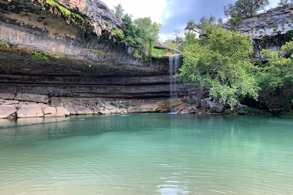 Photo of Hamilton Pool Preserve with green trees and waterfall.