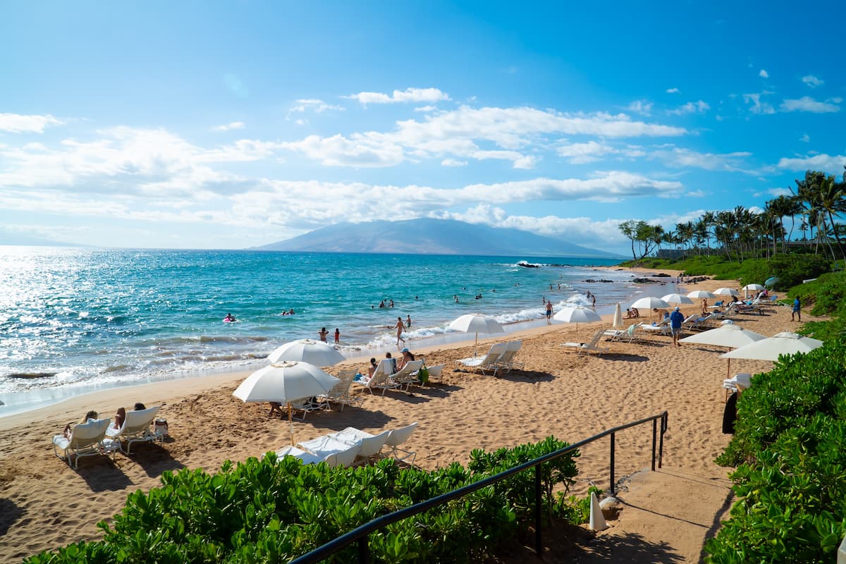 White sunbeds, white umbrellas, and people swimming at a beach in Maui, Hawaii. 