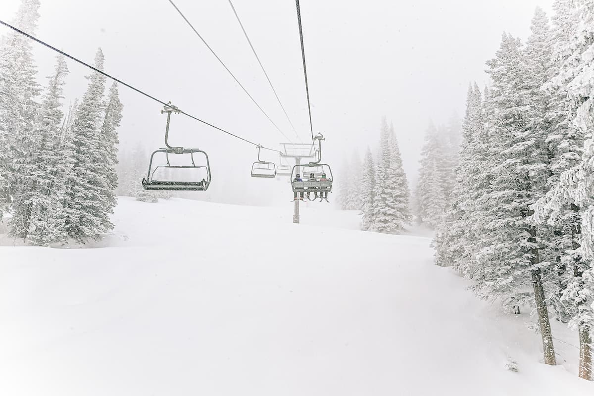Three people riding a ski cable car while snowing. 