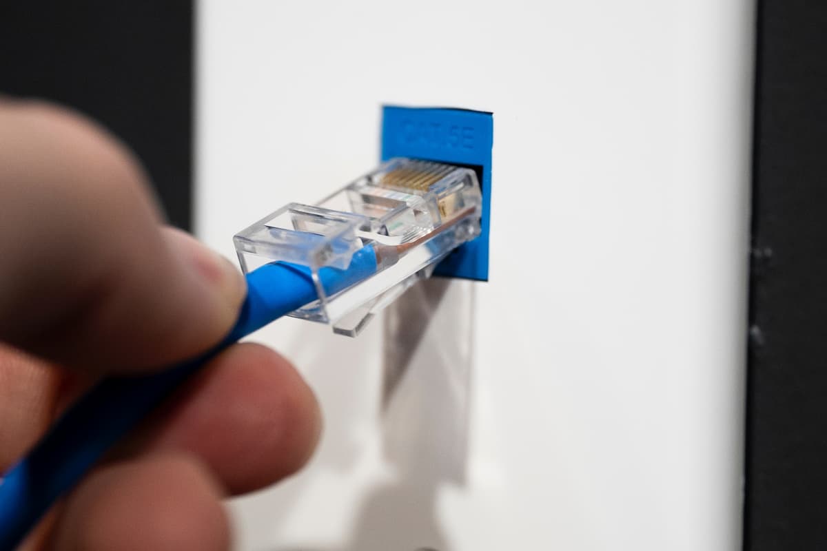A close-up photo of a person's hand holding an ethernet cable being plugged into a port.