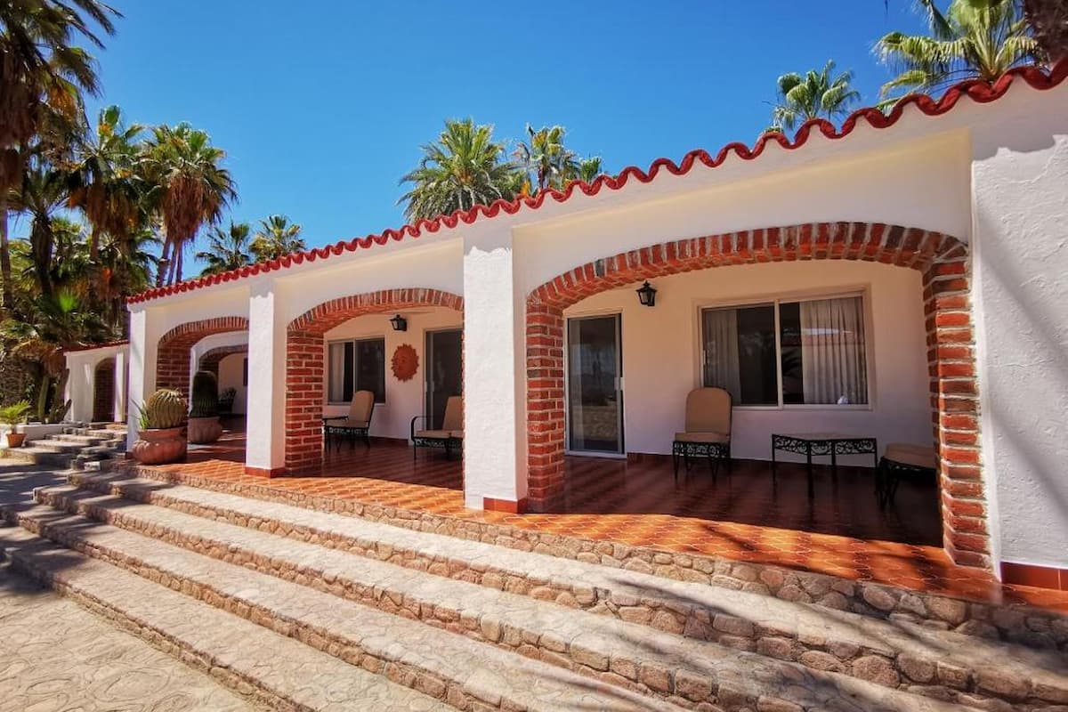 A white hotel with some red bricks, a red roof, and palm trees.