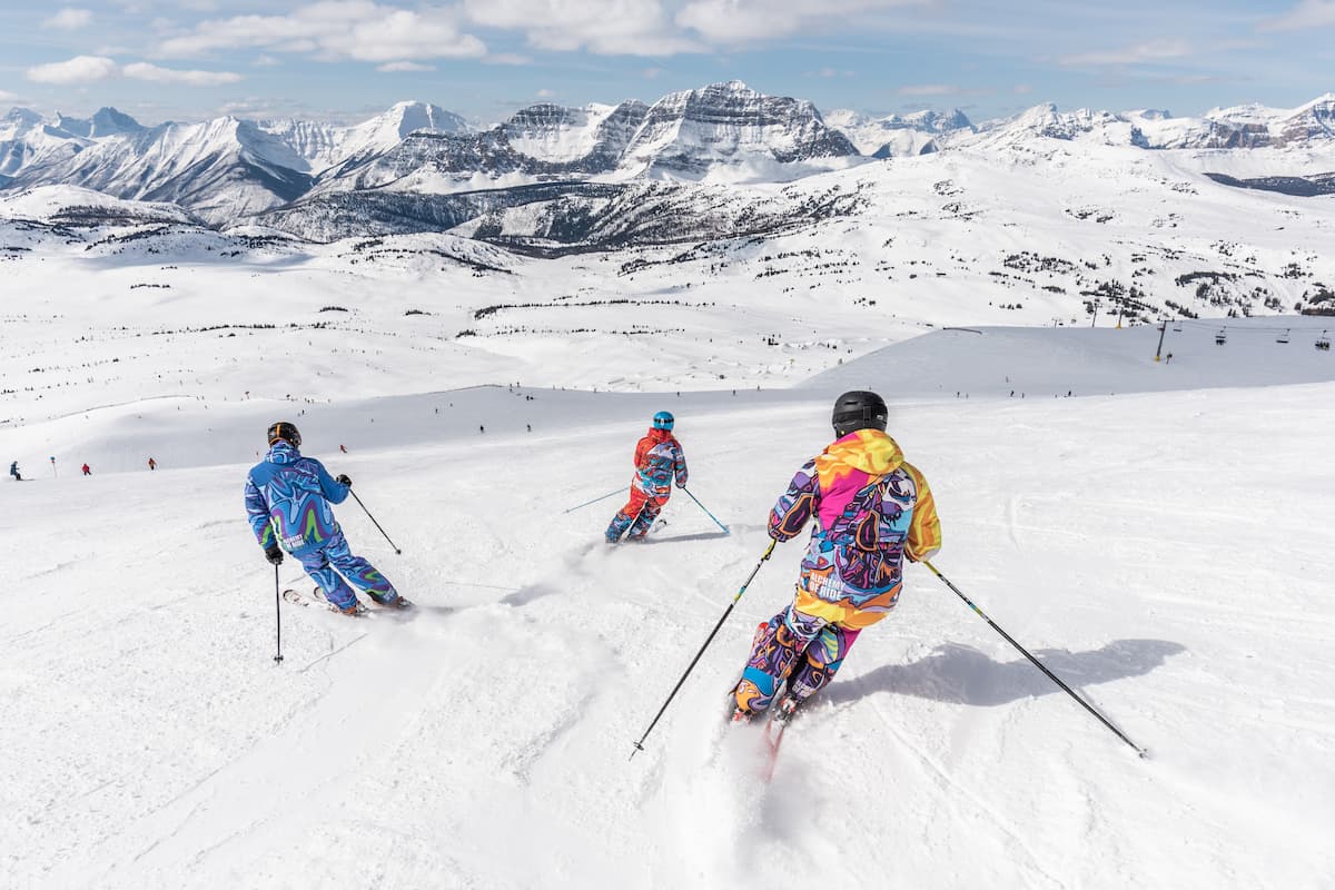 Three people skiing in a ski resort with a mountain view. 