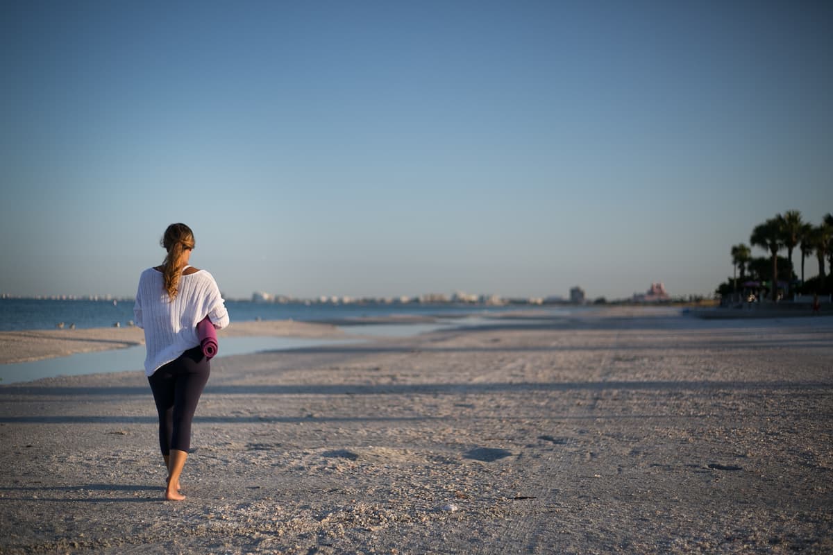 A woman holding a yoga mat while walking at the beach. 