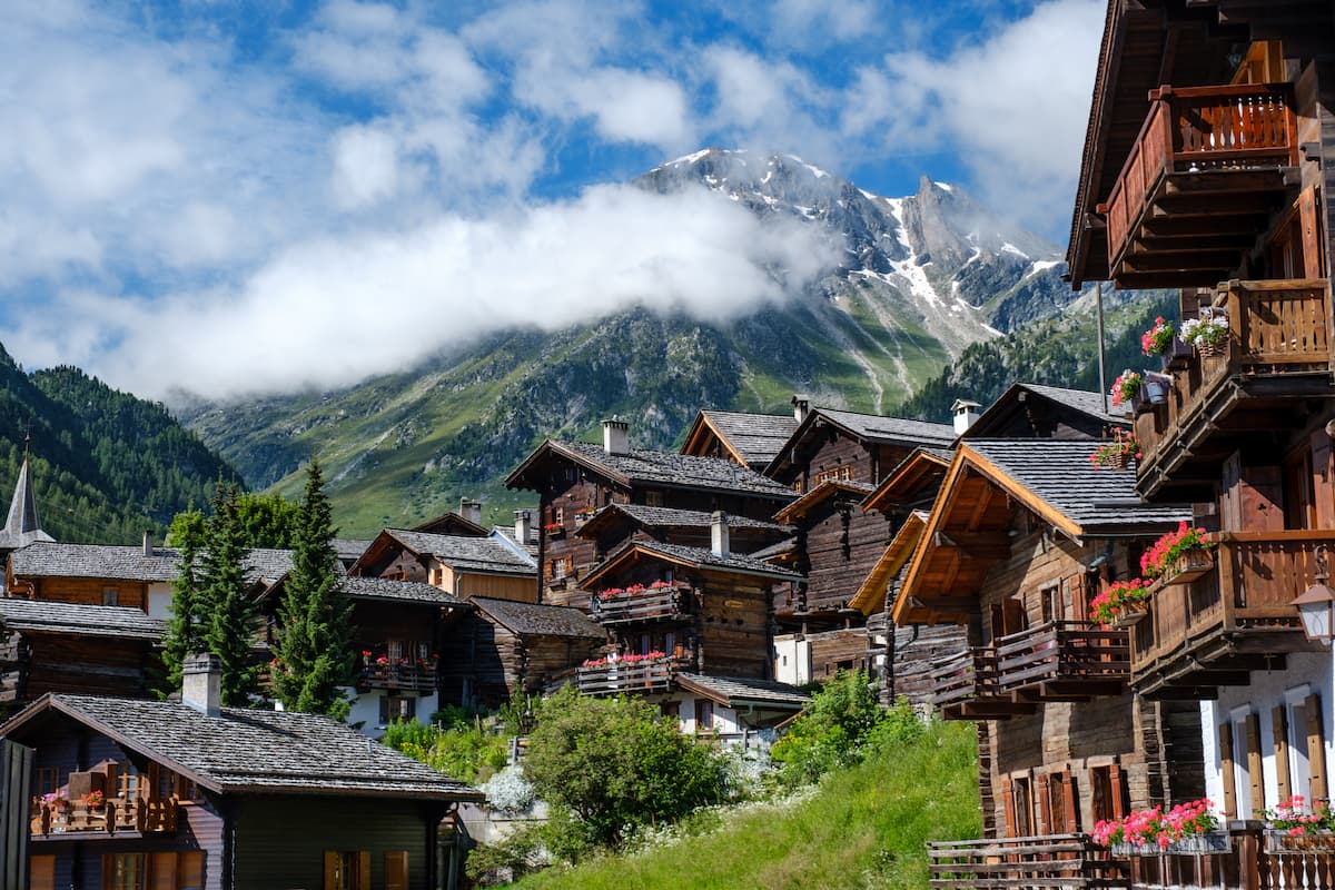 Wooden houses near green trees and mountains under white clouds during daytime. 